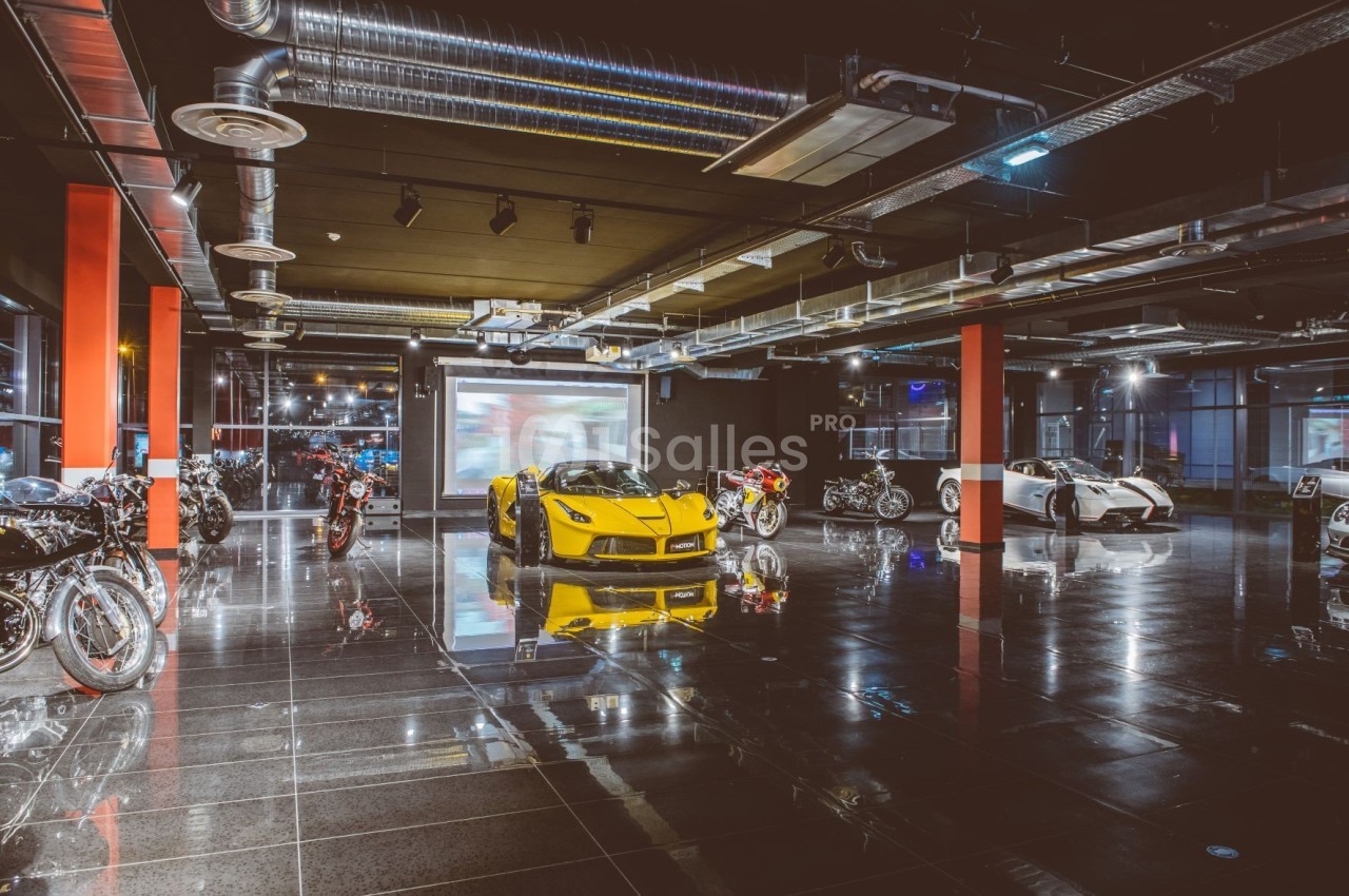 Salle d'exposition moderne avec voitures de sport et motos alignées sur un sol brillant sous un éclairage industriel.