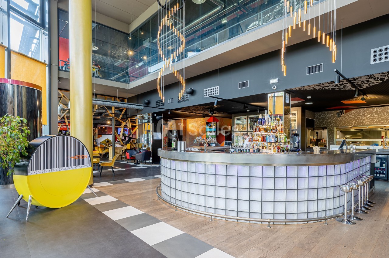Intérieur d'un bar moderne avec comptoir en verre rétroéclairé, mobilier design et éclairage suspendu.