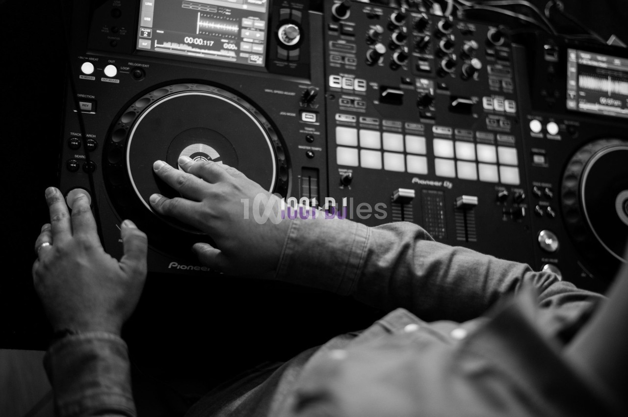 Un DJ manipule une platine de mixage dans un environnement sombre, capturé en noir et blanc.