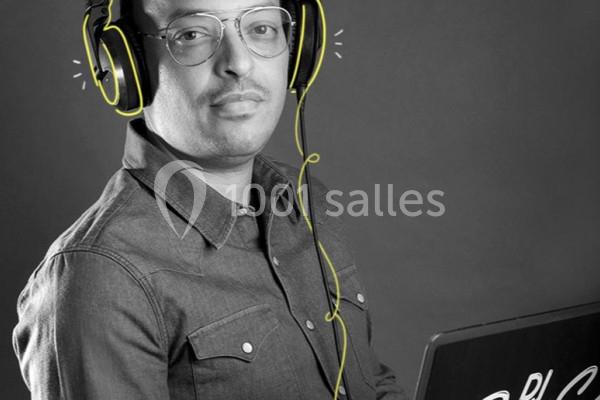 Homme portant un casque audio, regardant l'objectif, assis devant un ordinateur portable dans un décor sobre.