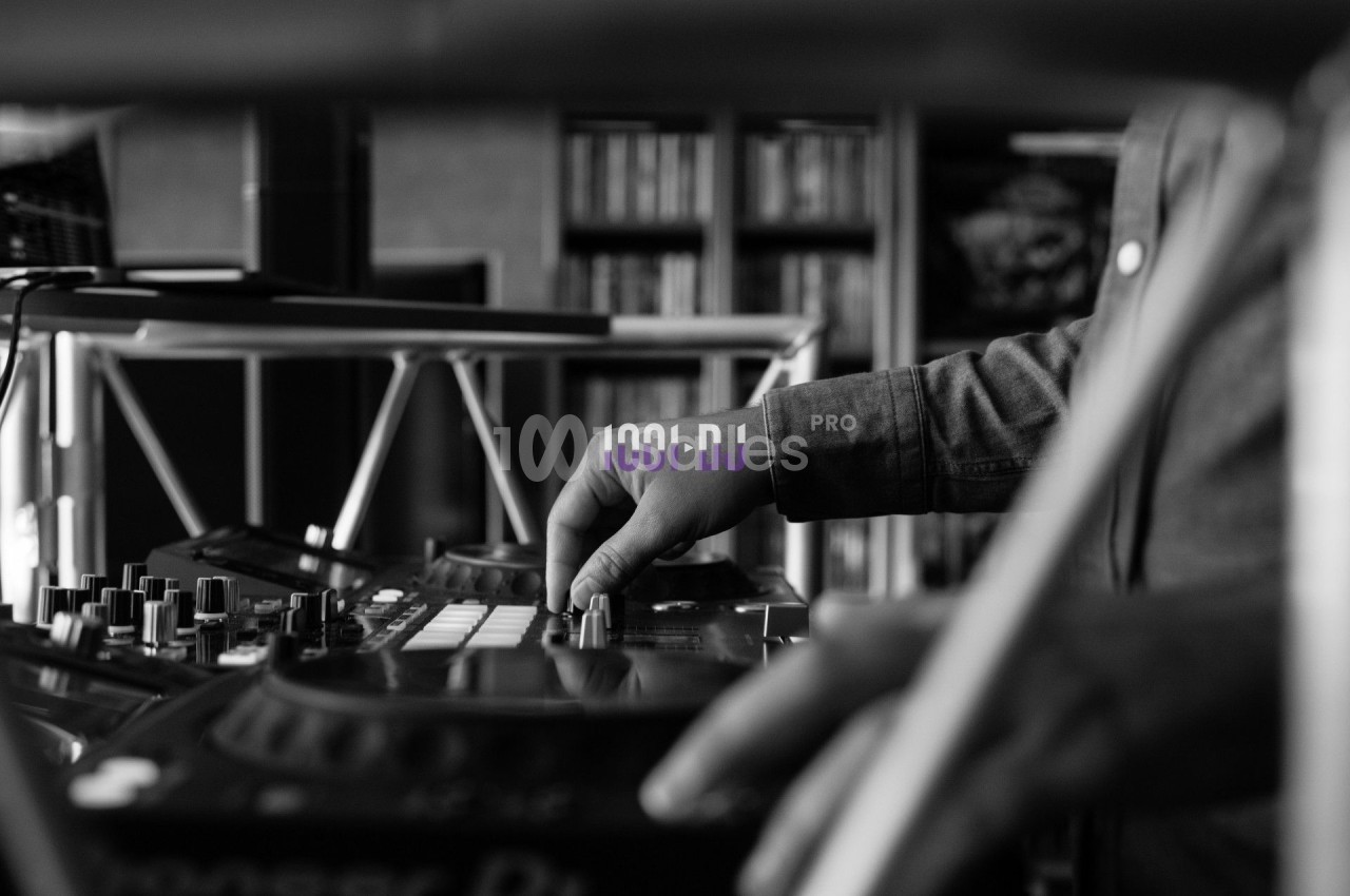 Un DJ ajuste les commandes d'une table de mixage dans un environnement intérieur, en noir et blanc.