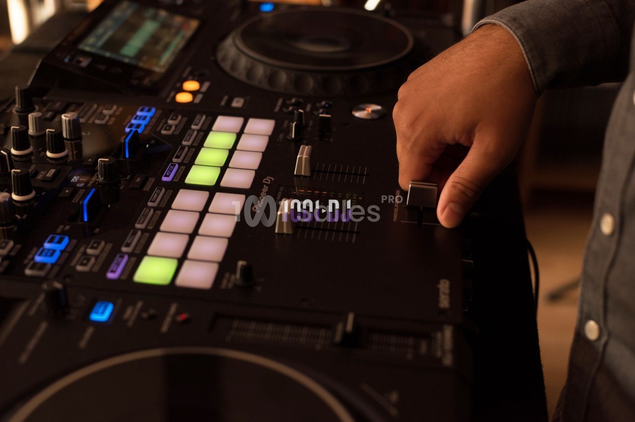 Main d'une personne ajustant un curseur sur une console de mixage DJ avec des boutons et lumières colorées.