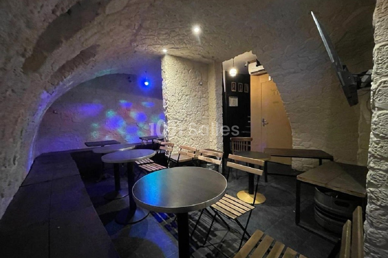 Salle voûtée en pierre avec tables, chaises en bois et éclairage tamisé, décorée de points lumineux colorés.