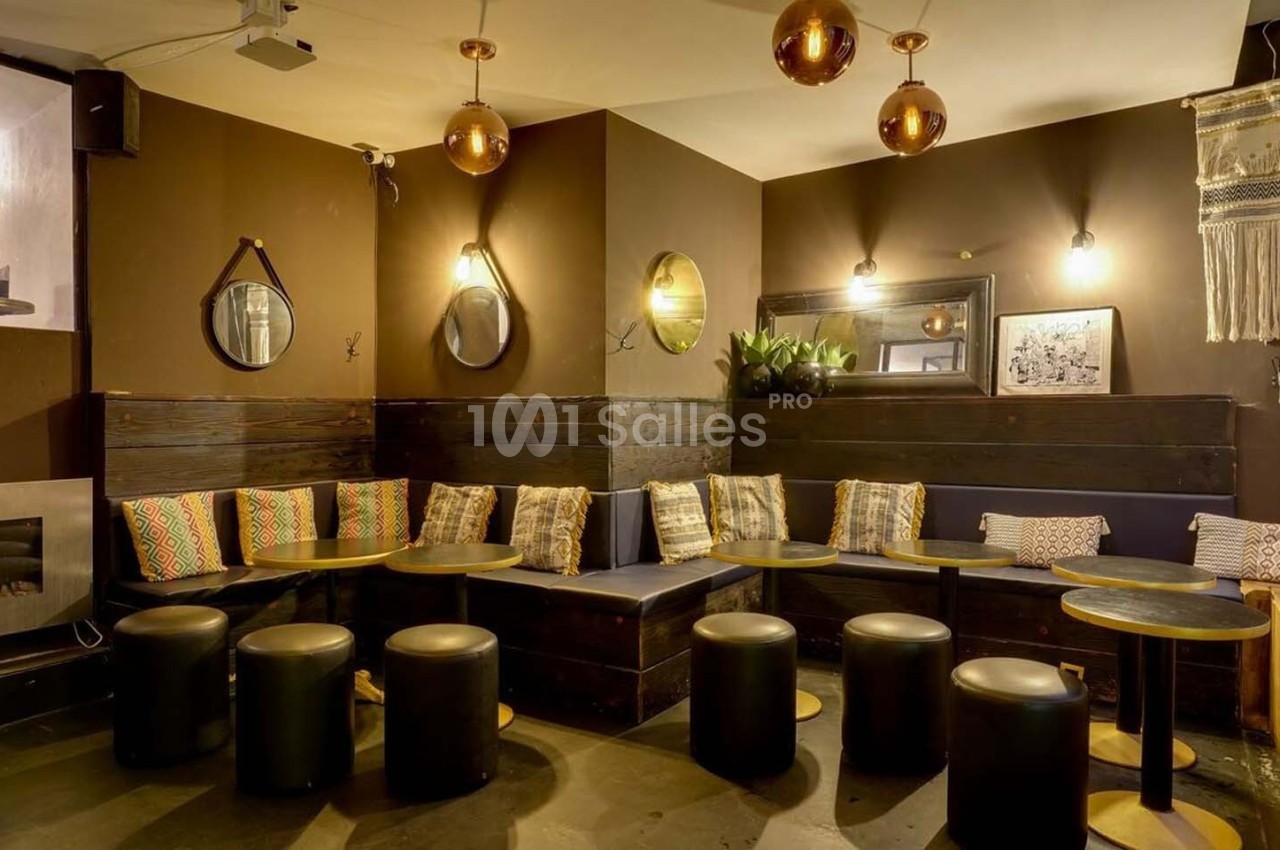 Espace intérieur chaleureux avec banquettes, coussins colorés, tables basses et luminaires suspendus en cuivre.