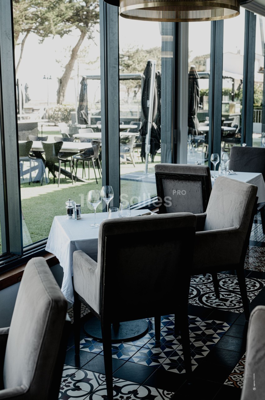 Salle de restaurant élégante avec tables dressées, grandes baies vitrées et vue sur une terrasse extérieure.