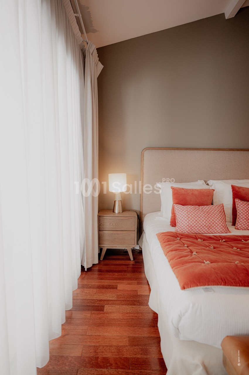 Chambre lumineuse avec lit double, couvre-lit orange, coussins assortis, table de chevet en bois et lampe allumée.