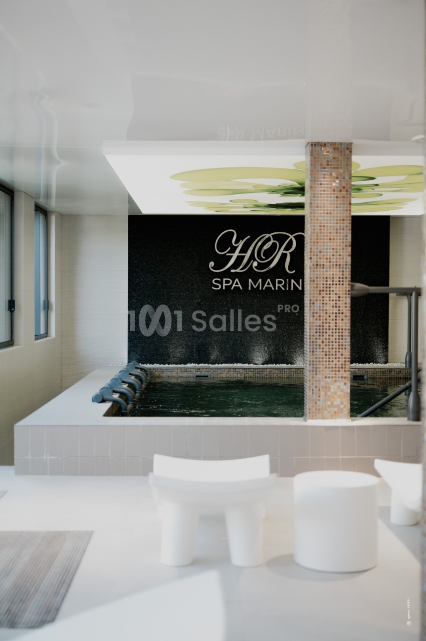 Piscine intérieure d'un spa avec mosaïques, jets d'eau et mur noir portant l'inscription ’HR Spa Marin’.