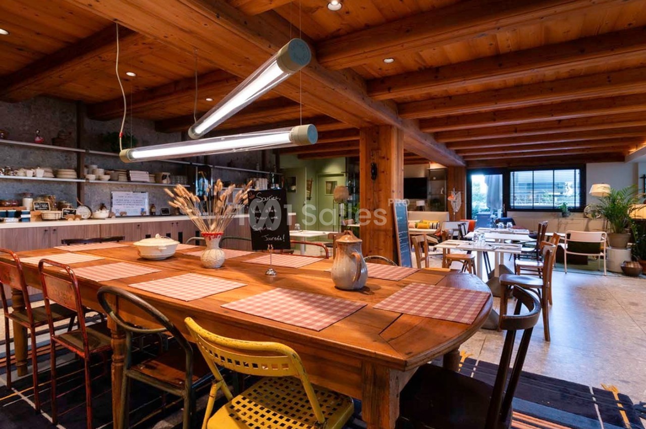 Salle à manger chaleureuse avec grande table en bois, chaises dépareillées, éclairage suspendu et ambiance rustique.
