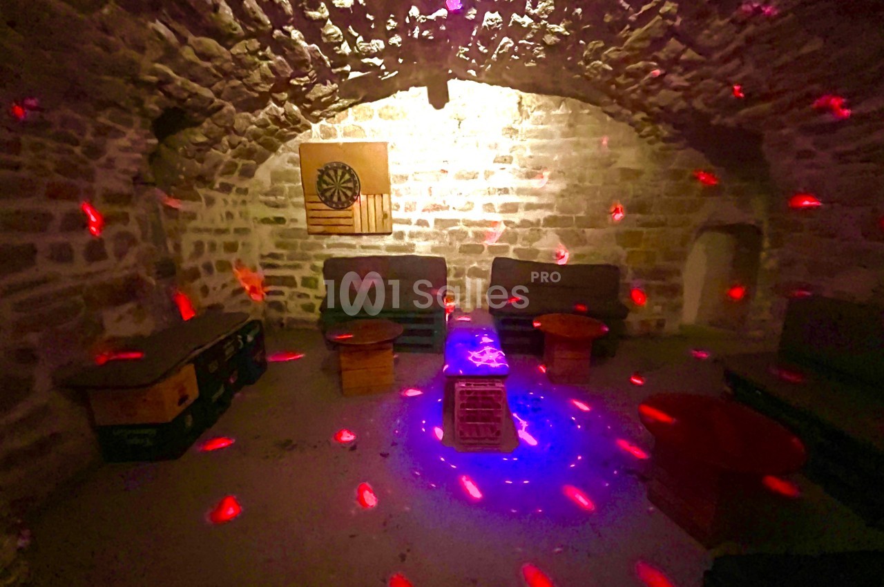 Salle voûtée en pierre avec des canapés, des tables basses et des lumières rouges projetées au plafond et sur les murs.