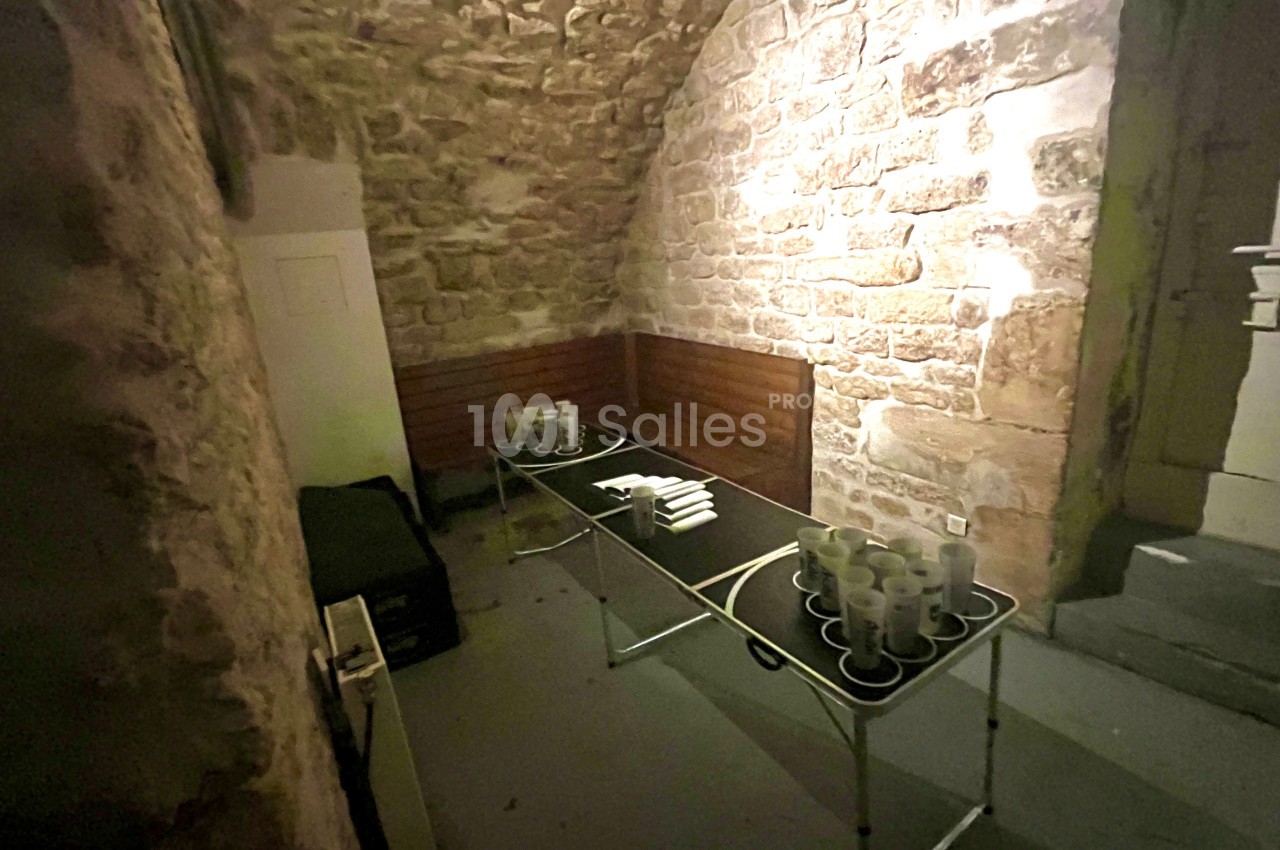 Table pliante avec tasses et serviettes dans une pièce voûtée aux murs en pierre éclairée par une lumière douce.