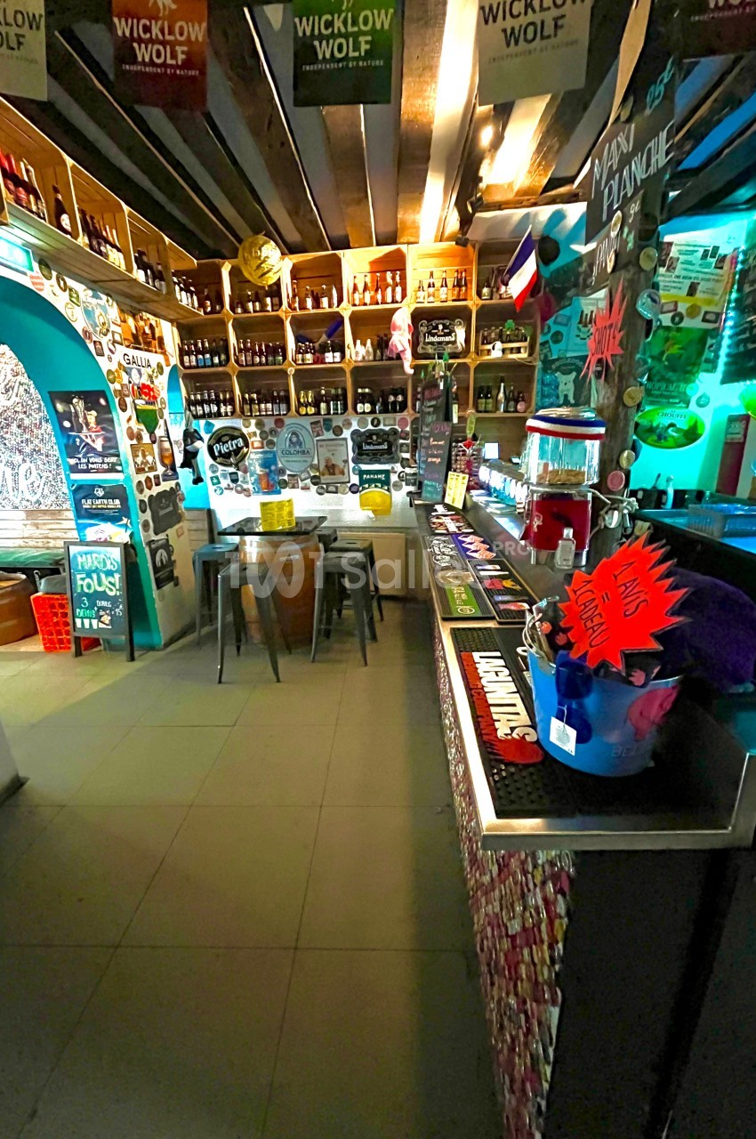 Intérieur d'un bar coloré avec étagères remplies de bouteilles, comptoir décoré et ambiance chaleureuse.