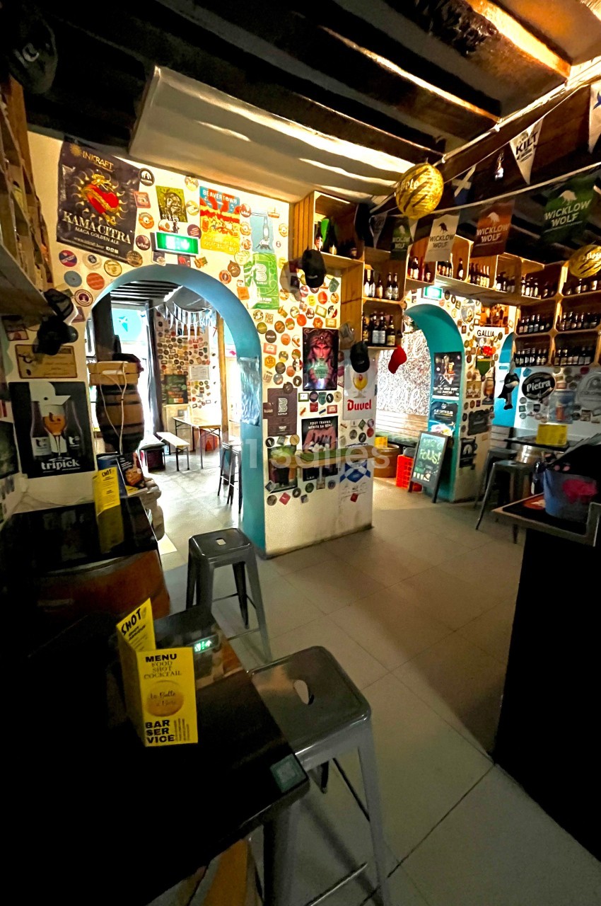 Intérieur d'un bar décoré d'affiches et d'autocollants, avec des étagères remplies de bouteilles et des tabourets…