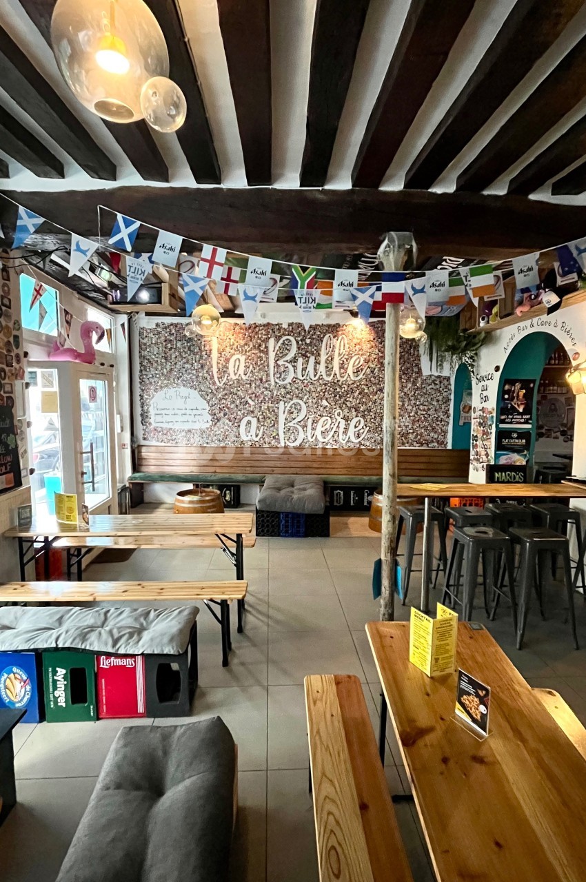 Intérieur d'un bar avec tables en bois, guirlandes de drapeaux et une enseigne murale ’La Bulle à Bière’.