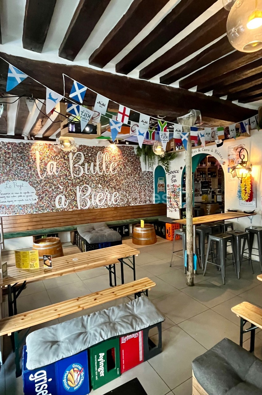 Intérieur d'un bar avec des tables en bois, des drapeaux suspendus et une décoration murale colorée.
