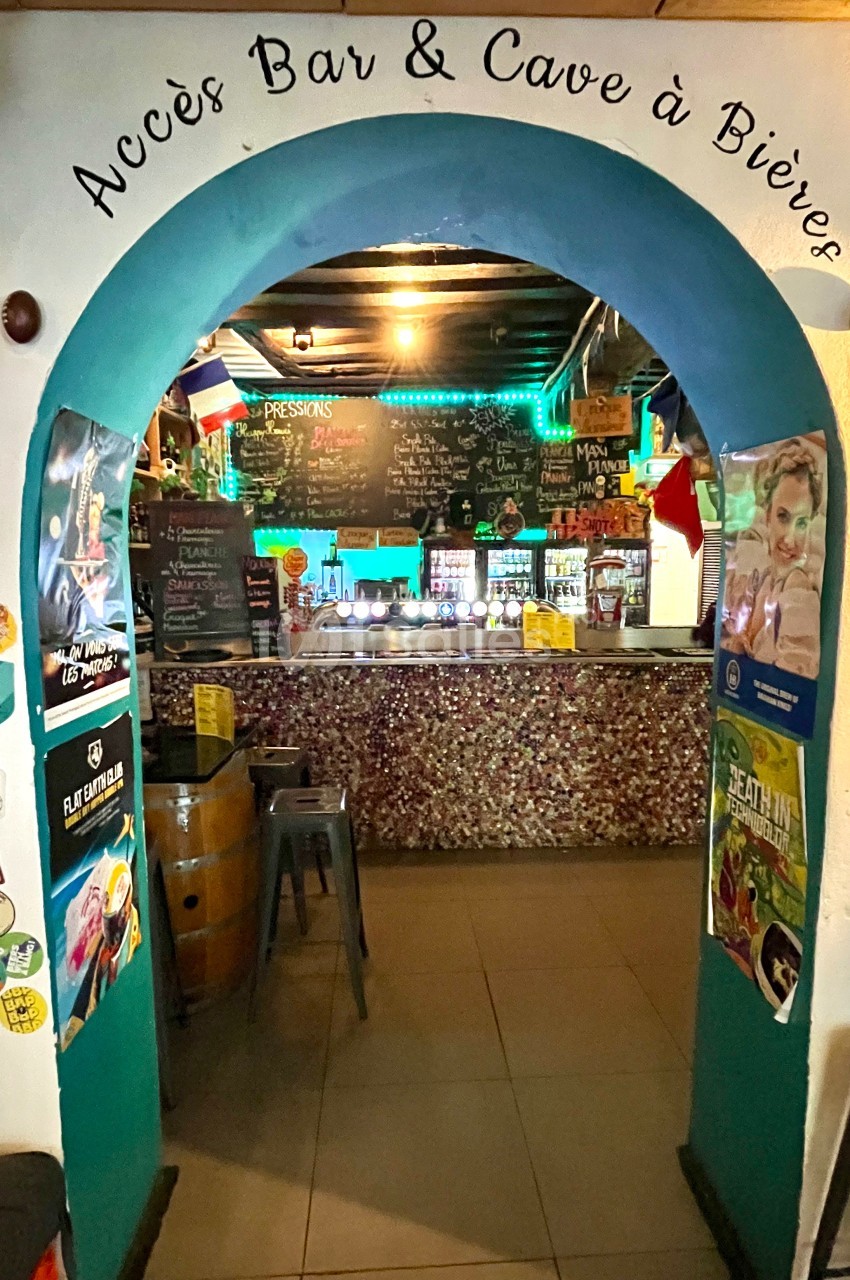 Entrée voûtée menant à un bar décoré avec des affiches, des lumières colorées et un comptoir en mosaïque.