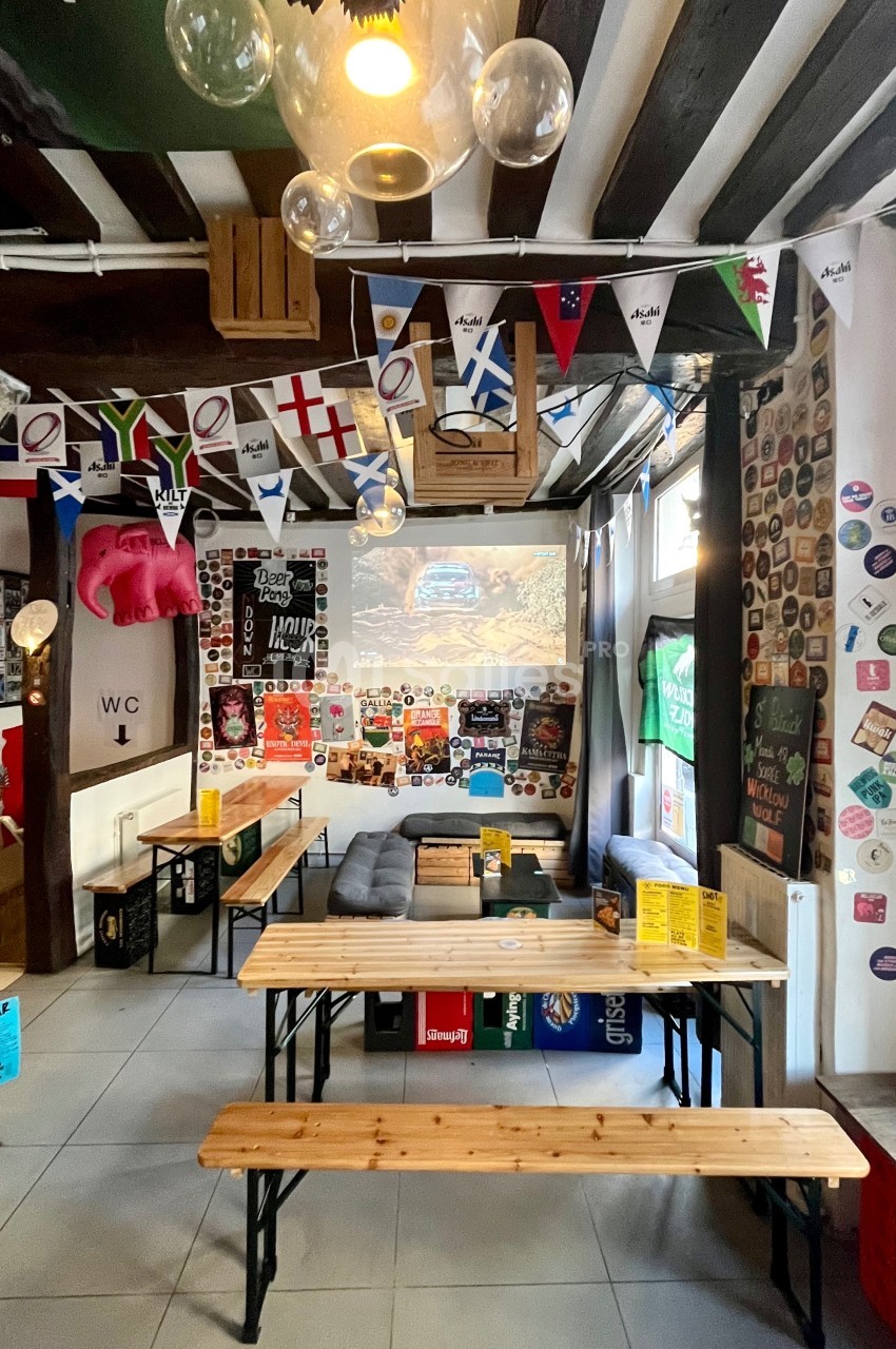 Salle conviviale décorée de fanions, affiches et objets variés, avec tables en bois et un écran projetant une image.