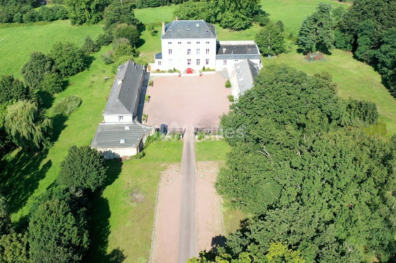 Vue aérienne d'une grande propriété avec un bâtiment principal, des dépendances et une cour entourée de verdure.