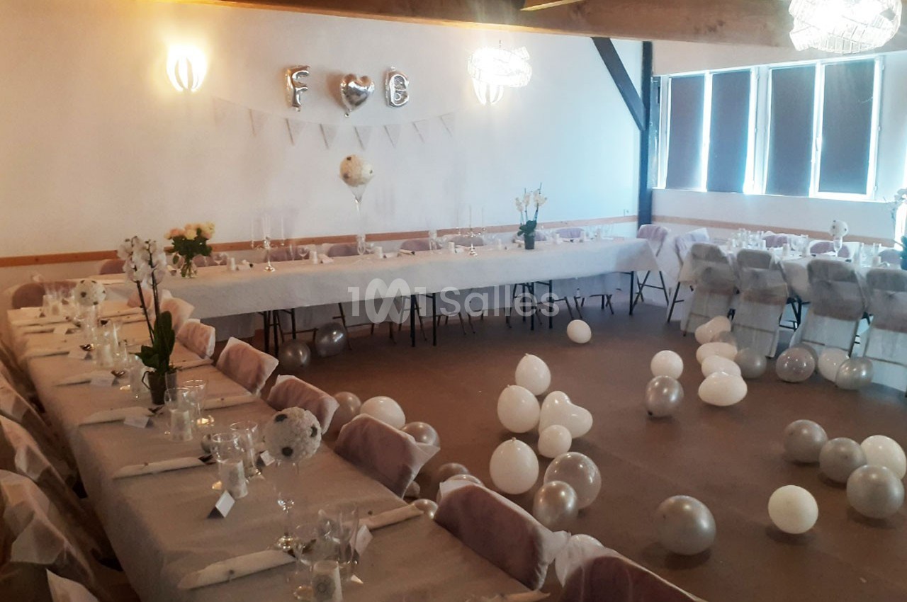 Salle décorée pour un événement avec tables dressées, ballons blancs au sol et guirlande de lettres argentées.