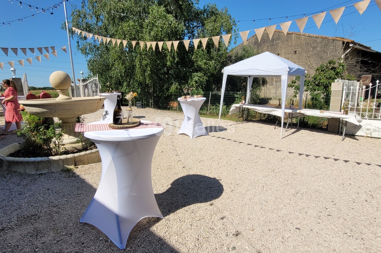 Cour extérieure décorée pour un événement avec tables hautes, guirlandes de fanions et tonnelle blanche.