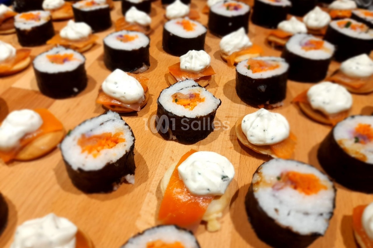 Assortiment de sushis et de bouchées au saumon garnies de crème, disposés sur une planche en bois.