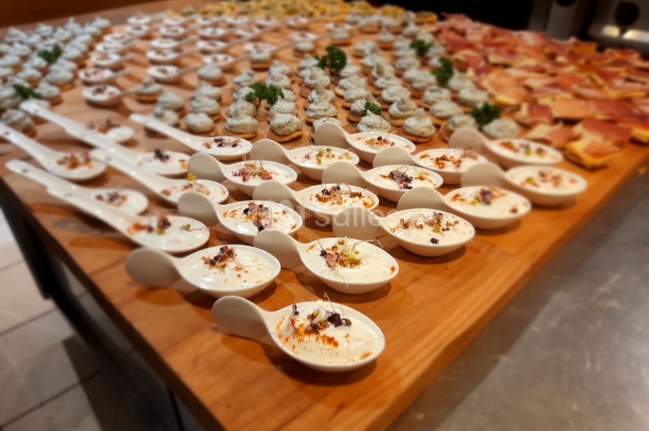 Assortiment de bouchées apéritives disposées sur une table en bois, incluant des cuillères garnies et des toasts variés.