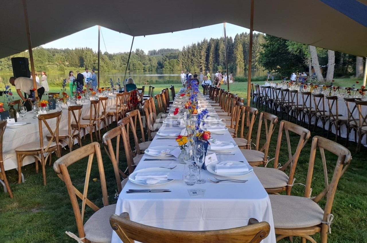 Tables dressées en extérieur sous une tente, avec nappes blanches, chaises en bois et bouquets de fleurs colorées.
