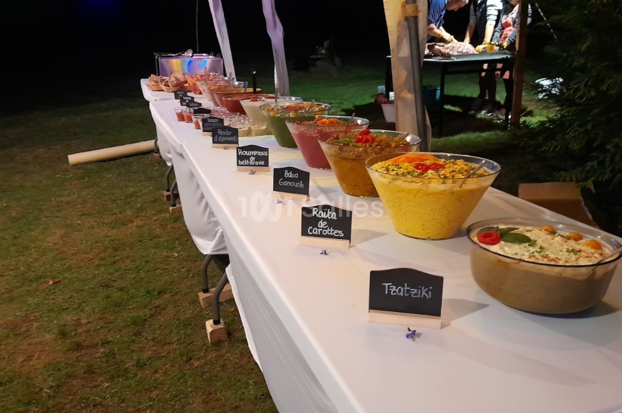 Buffet en extérieur avec une table garnie de salades variées, étiquettes descriptives et décoration simple.