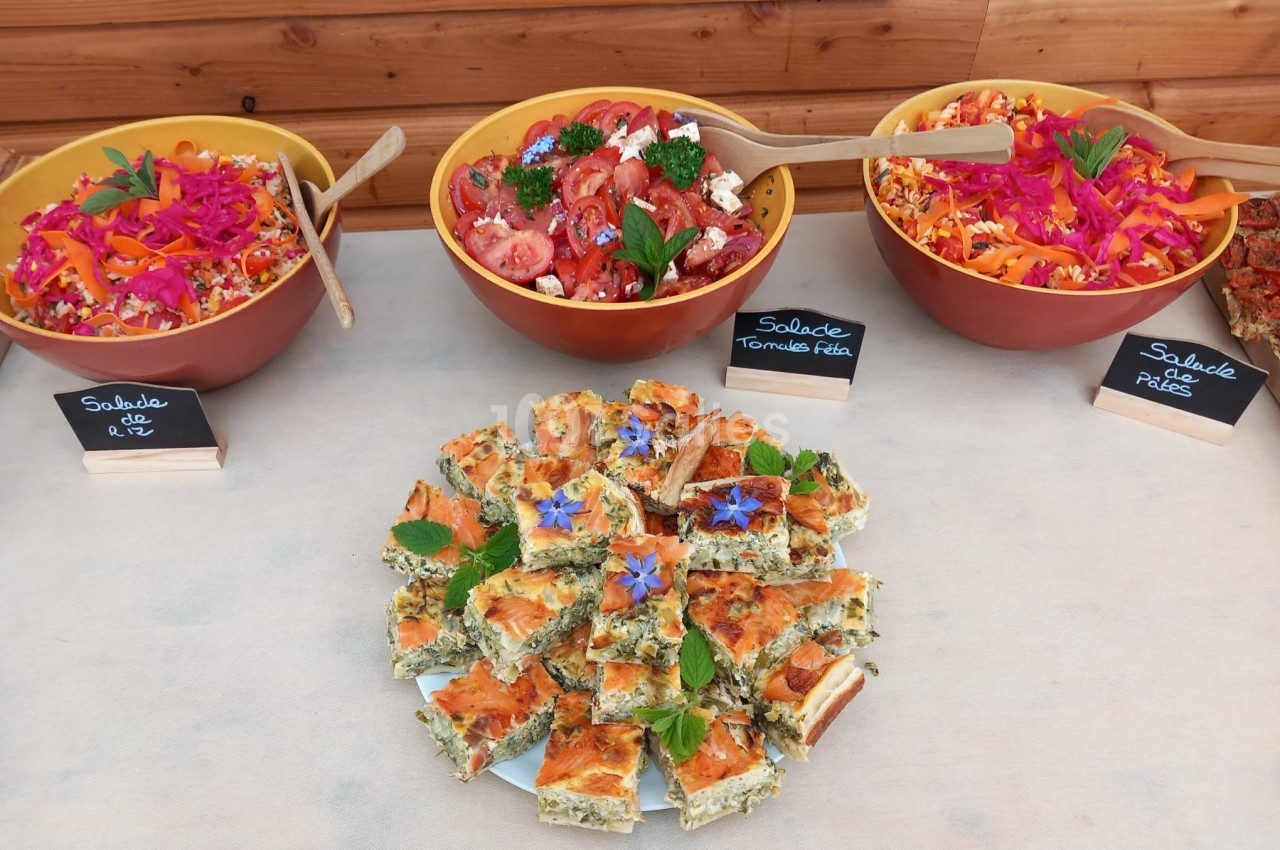 Trois salades colorées dans des bols et un plateau de quiche garnie de fleurs comestibles sur une table.