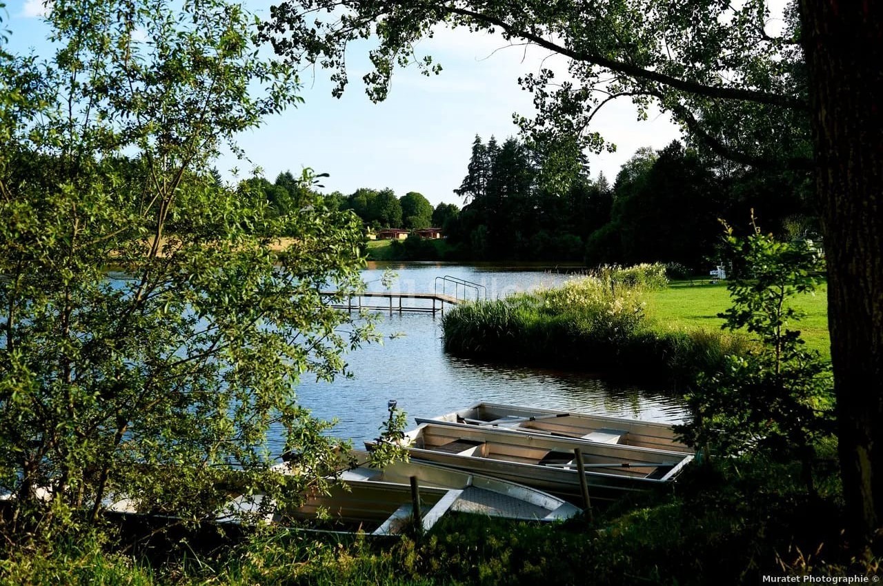 Barques amarrées au bord d'un lac entouré de verdure, avec un ponton en arrière-plan sous un ciel dégagé.