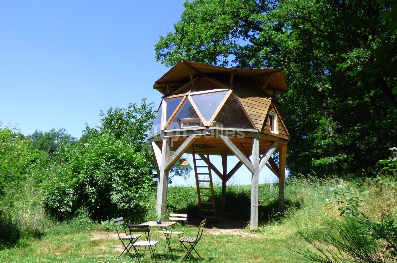 Cabane en bois sur pilotis entourée de verdure, avec une table et des chaises en plein air au premier plan.