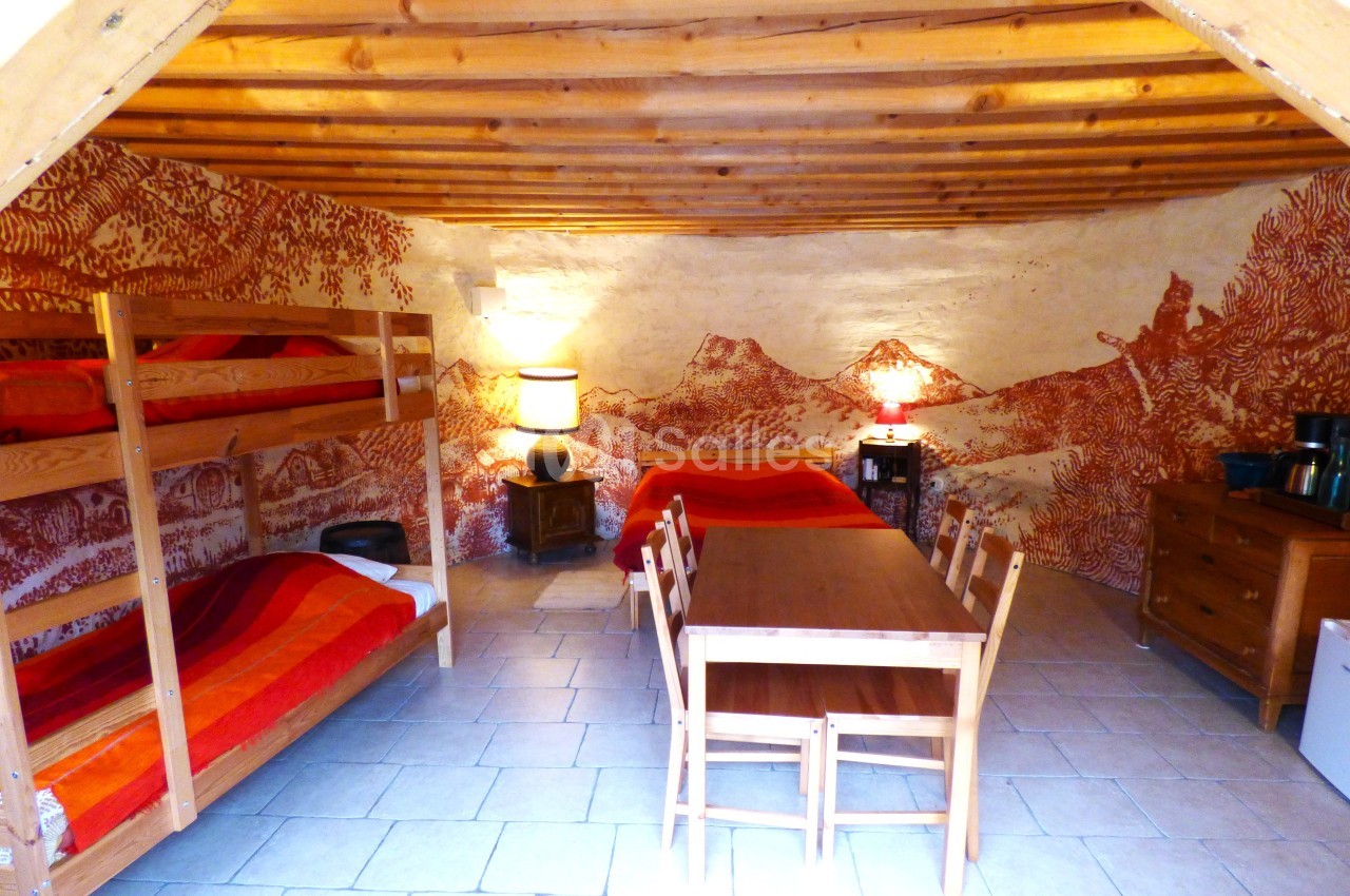 Chambre rustique avec lits superposés, lit double, table en bois et fresque murale représentant un paysage montagneux.