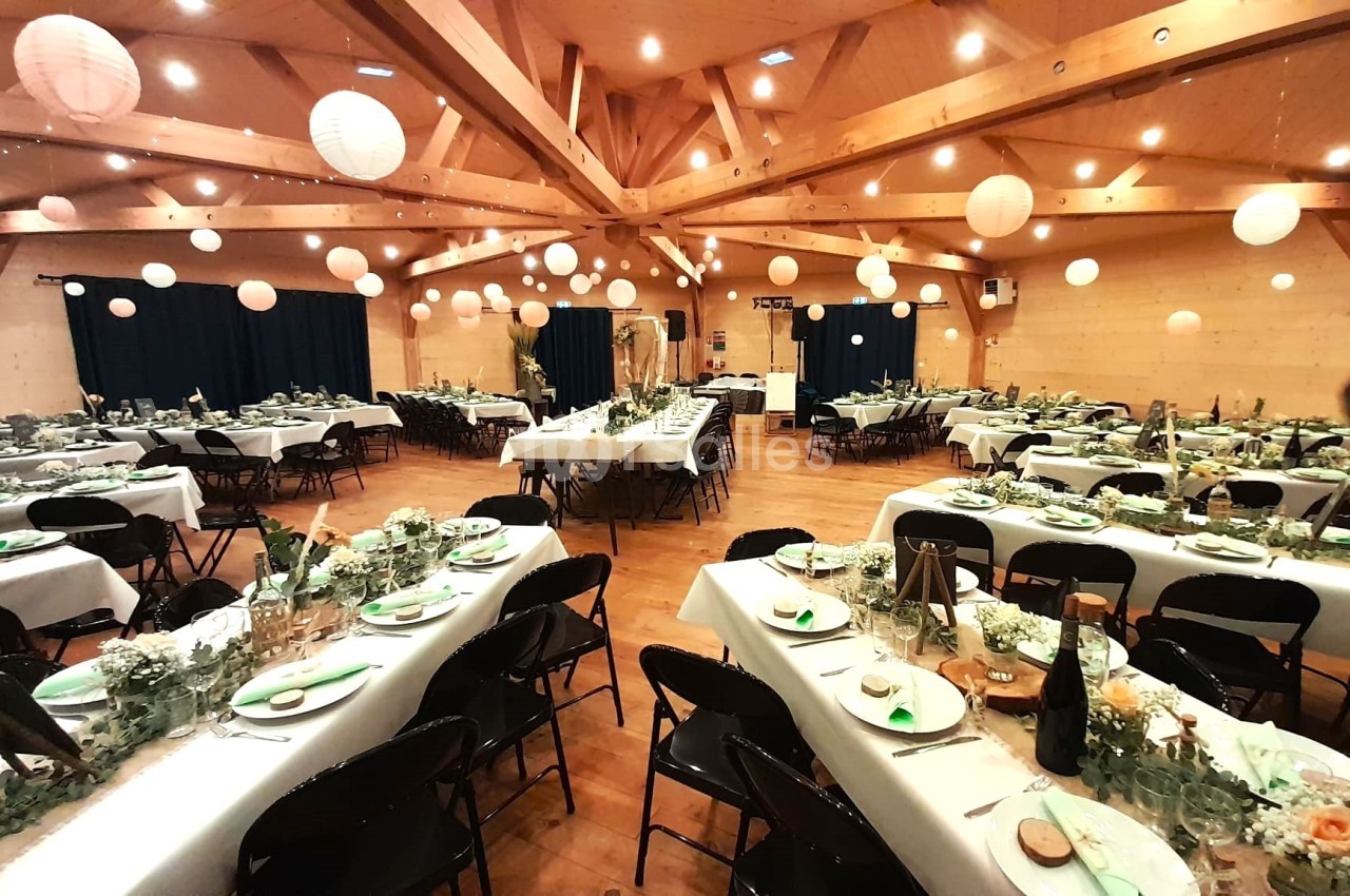 Salle de réception décorée pour un événement, avec tables dressées, guirlandes lumineuses et lanternes suspendues.
