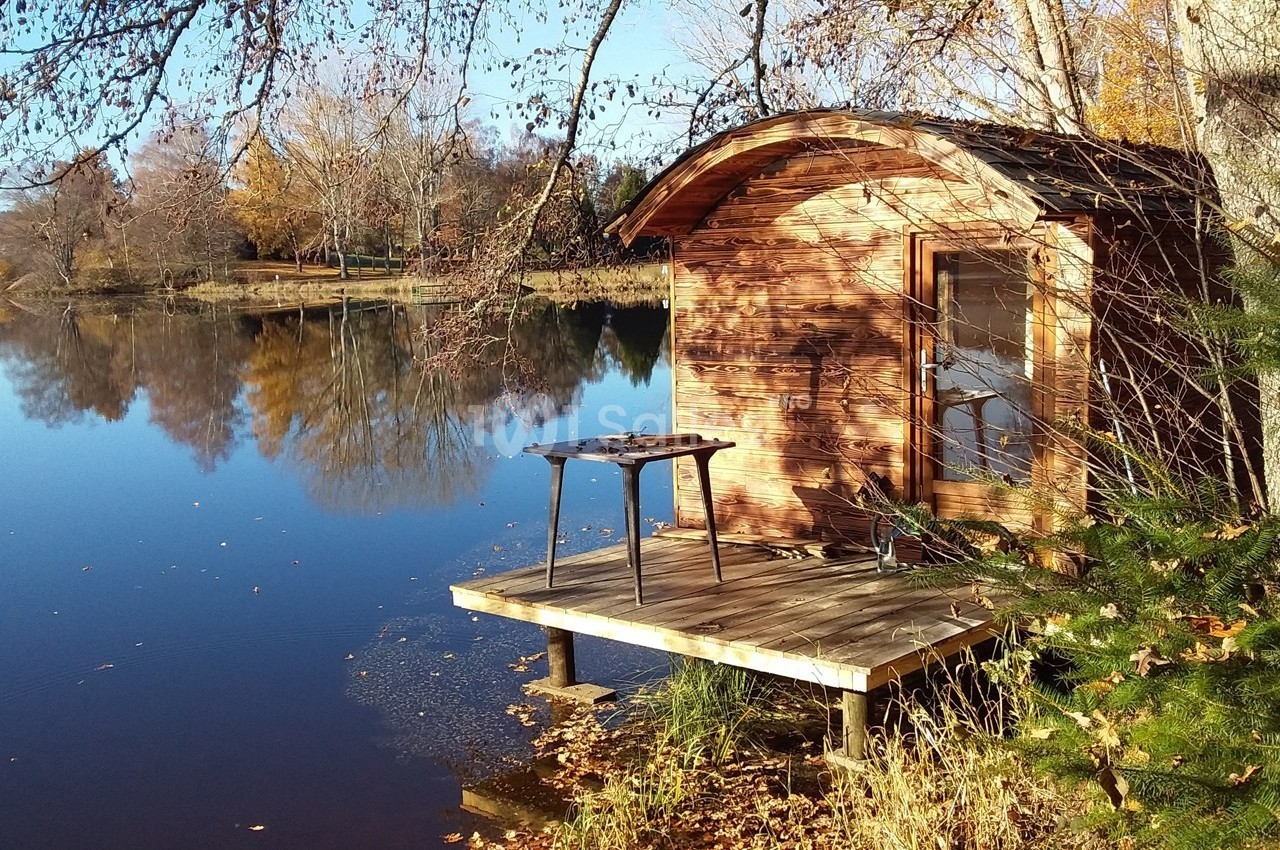 Cabane en bois au bord d'un lac calme entouré d'arbres aux couleurs automnales.