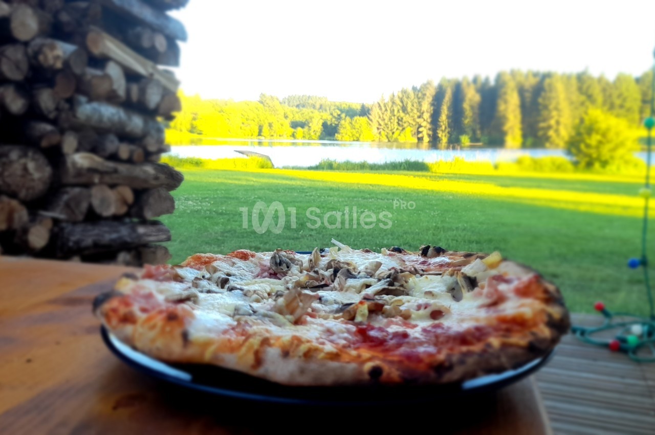 Pizza garnie de champignons et fromage sur une table en bois, avec vue sur un lac et une forêt en arrière-plan.