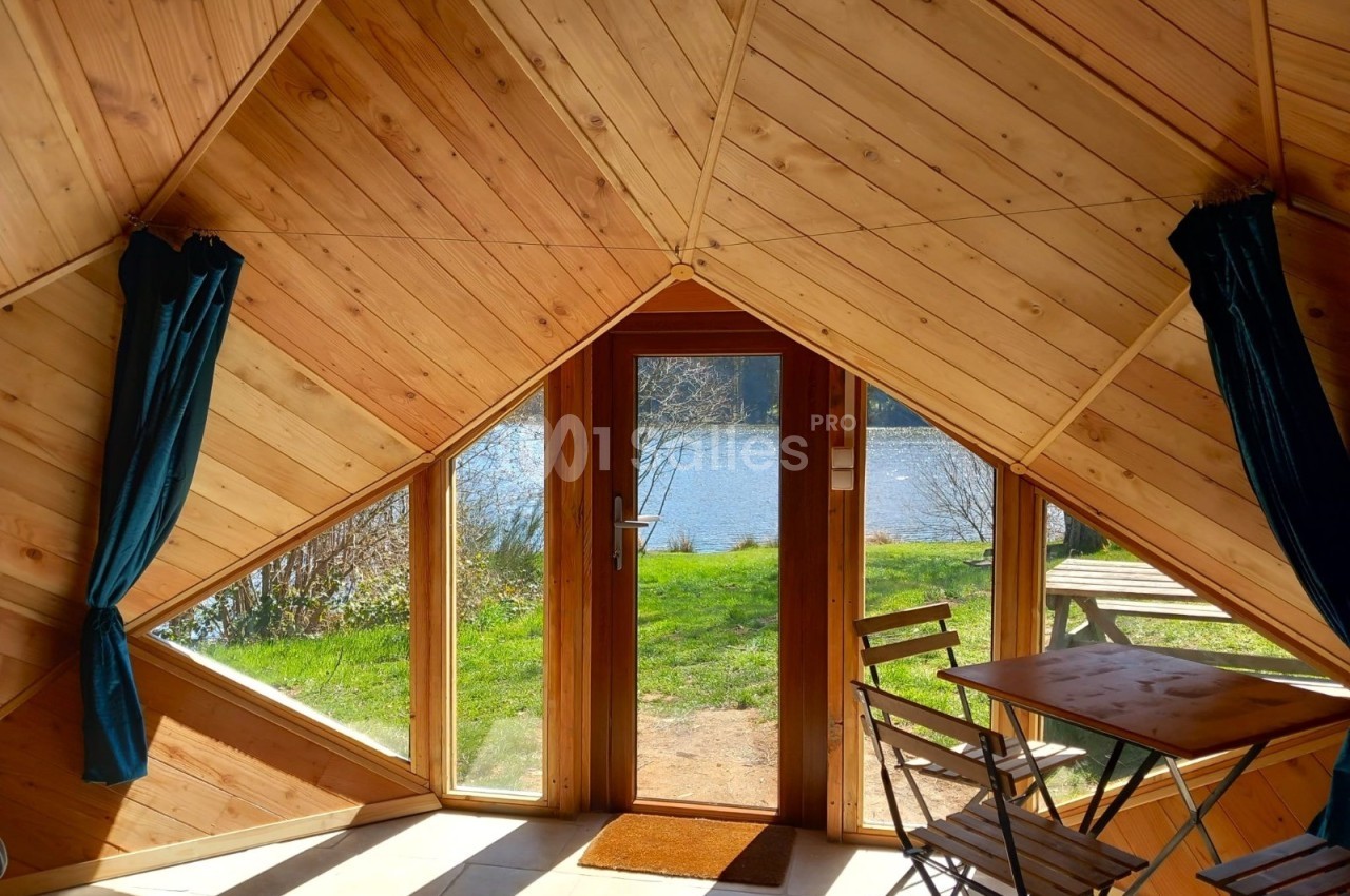 Vue intérieure d'une cabane en bois avec une porte vitrée donnant sur un lac et un espace extérieur verdoyant.