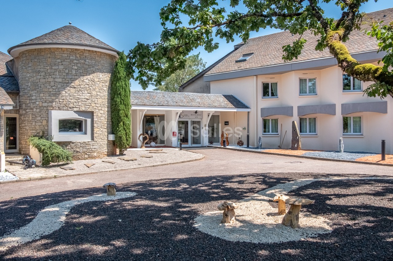 Entrée d'un bâtiment moderne avec façade en pierre et crépi, entouré d'arbres et d'un aménagement paysager.