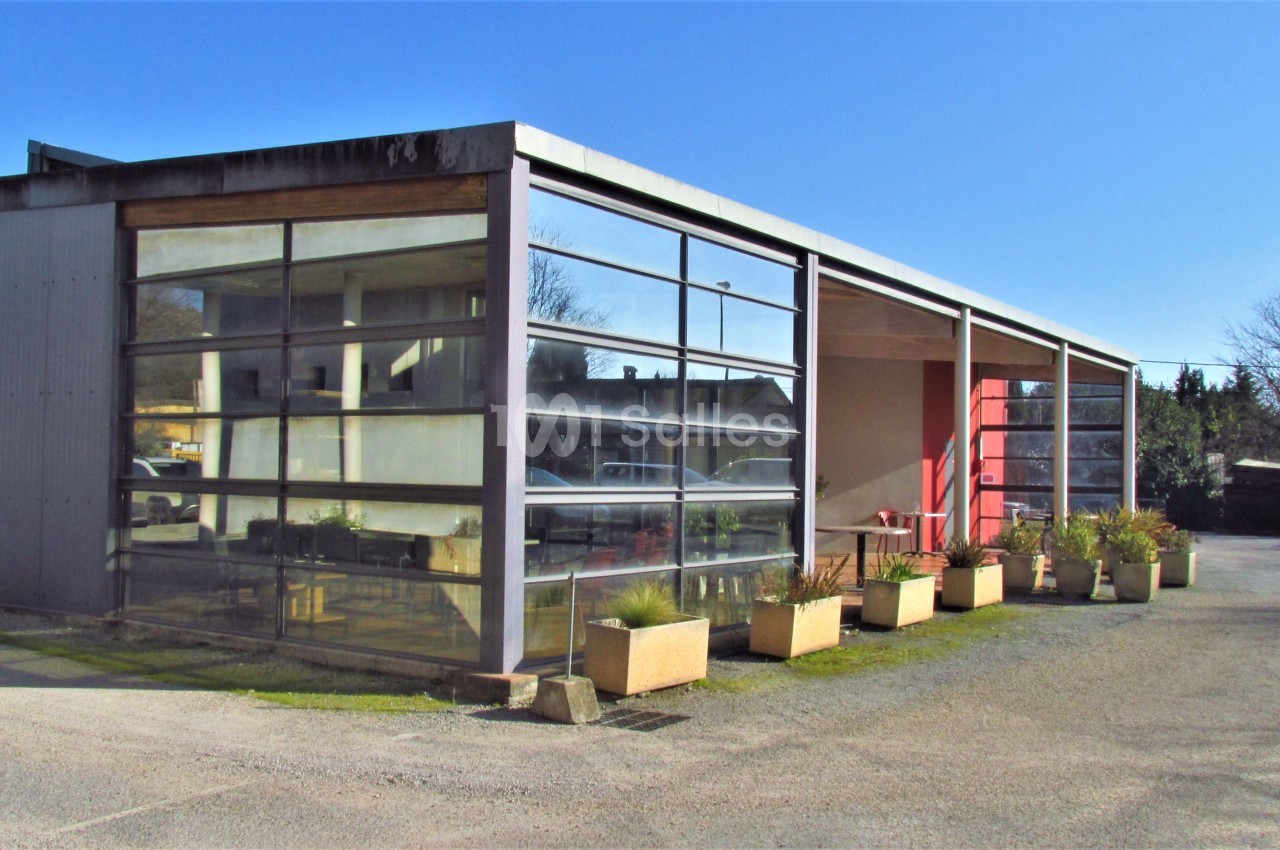 Bâtiment moderne avec façade vitrée, alignement de jardinières et ciel dégagé en arrière-plan.