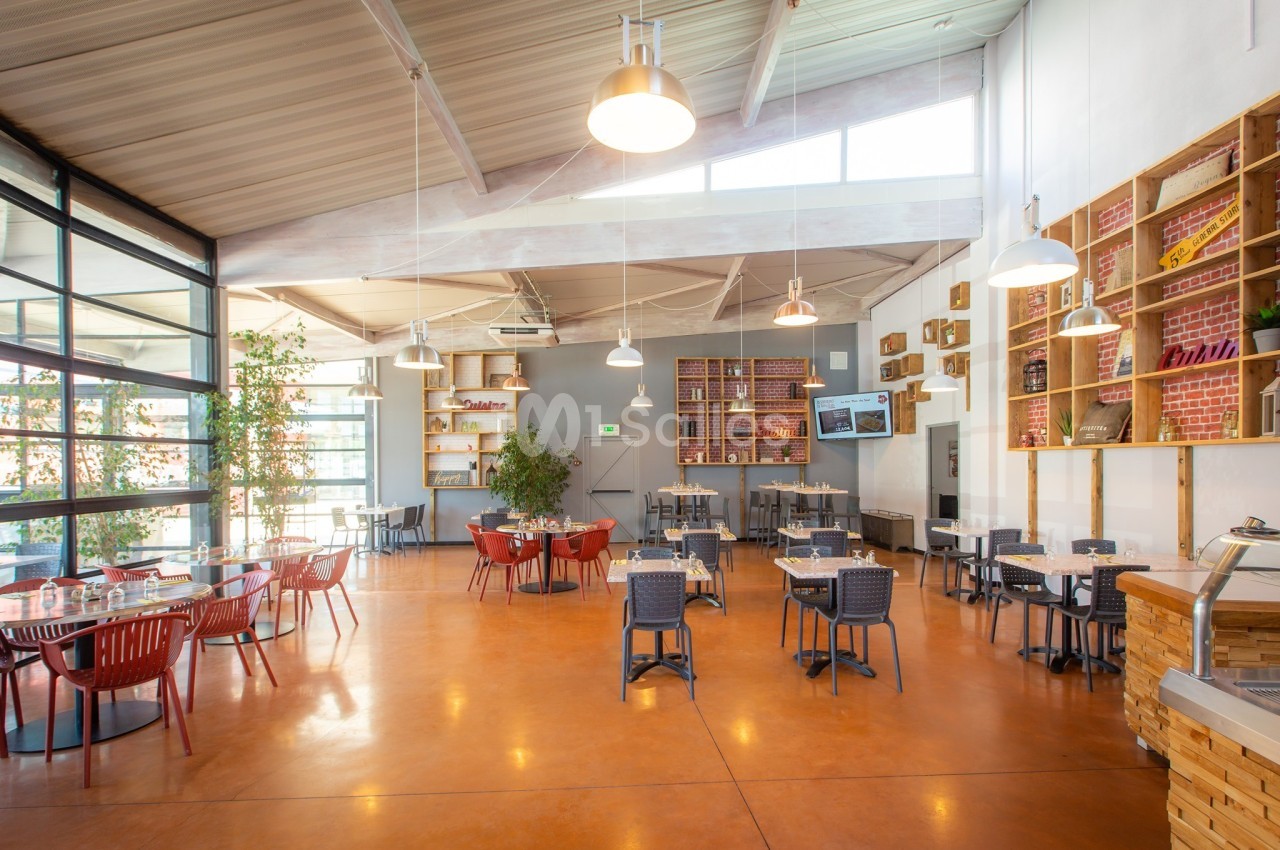 Salle de restaurant lumineuse avec tables espacées, chaises colorées et étagères décoratives sur les murs.