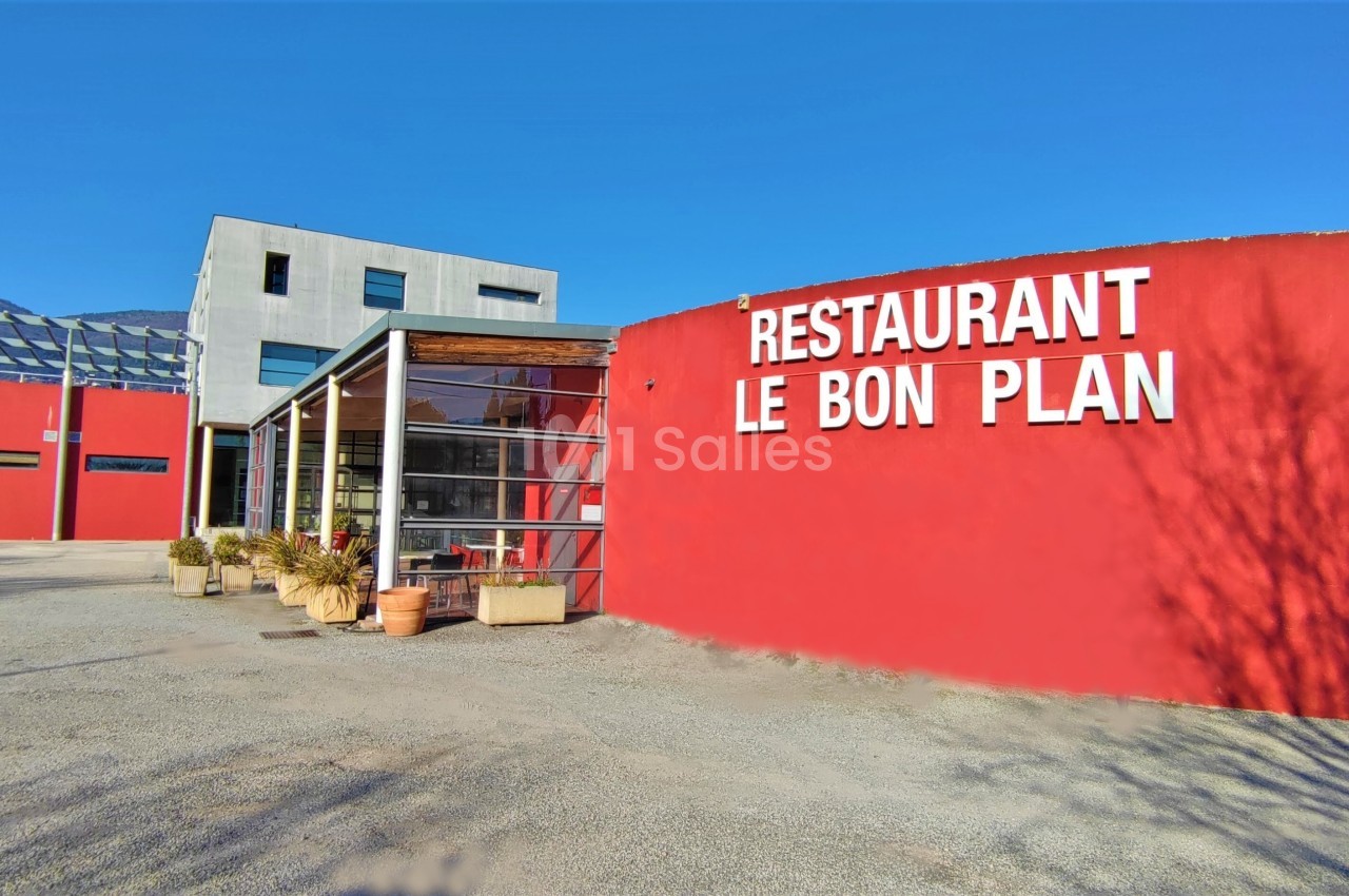 Façade d'un restaurant moderne avec murs rouges, grandes baies vitrées et inscription ’Restaurant Le Bon Plan’.