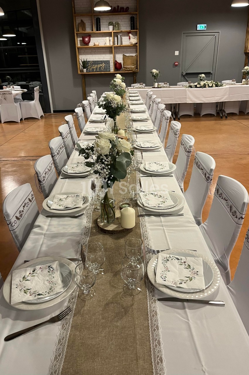 Table de réception décorée avec nappes blanches, chemins de table en lin, fleurs blanches et vaisselle élégante.