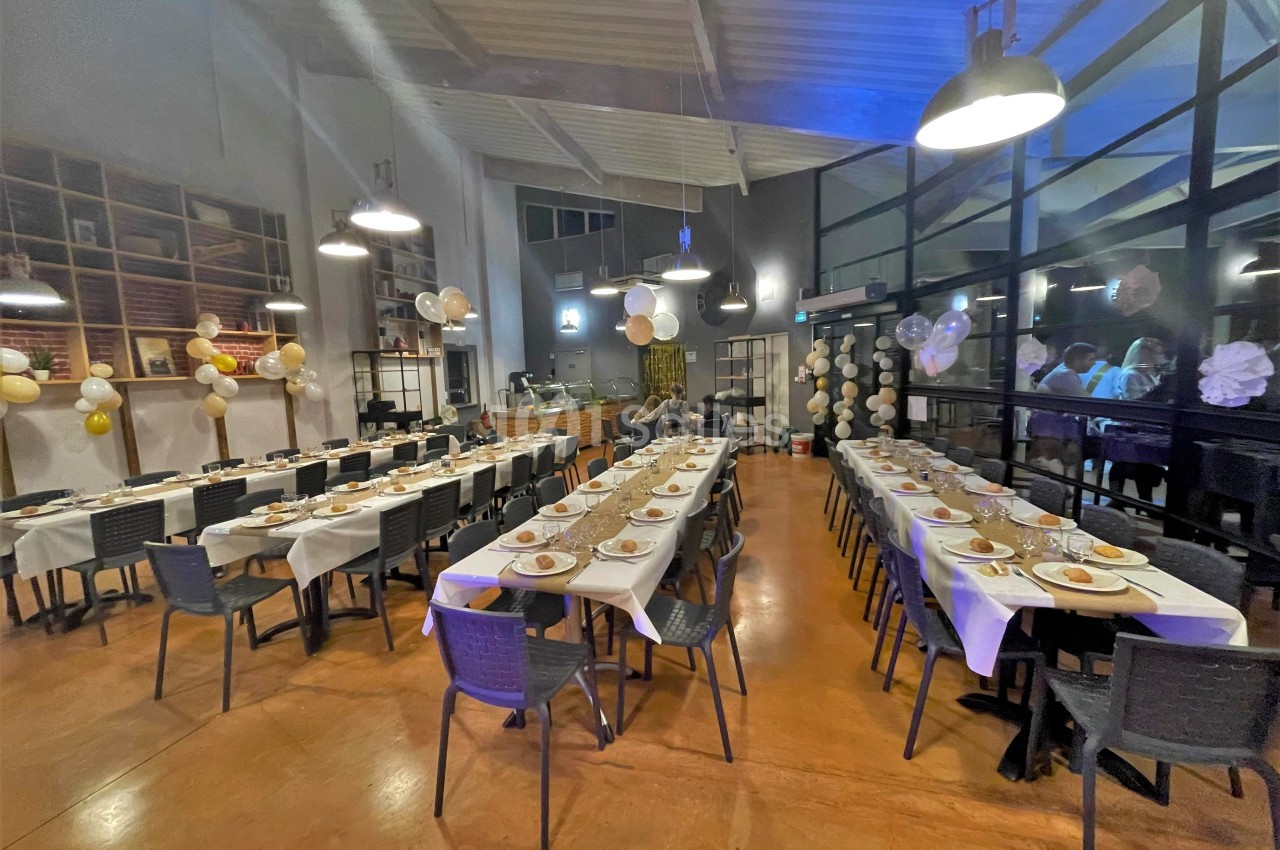 Salle décorée pour un événement, avec deux longues tables dressées, chaises noires et guirlandes suspendues.