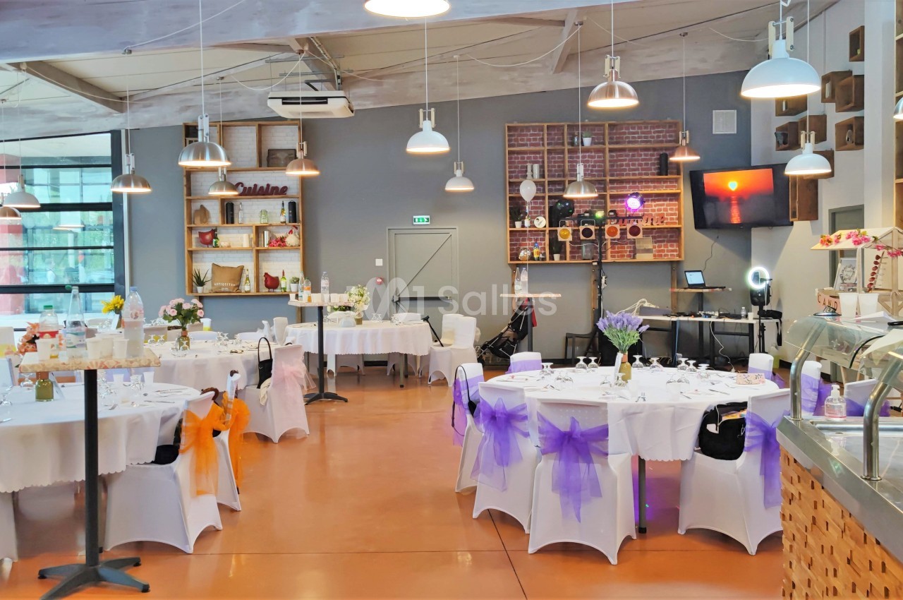 Salle de réception décorée avec des tables rondes, nappes blanches et chaises ornées de nœuds colorés.