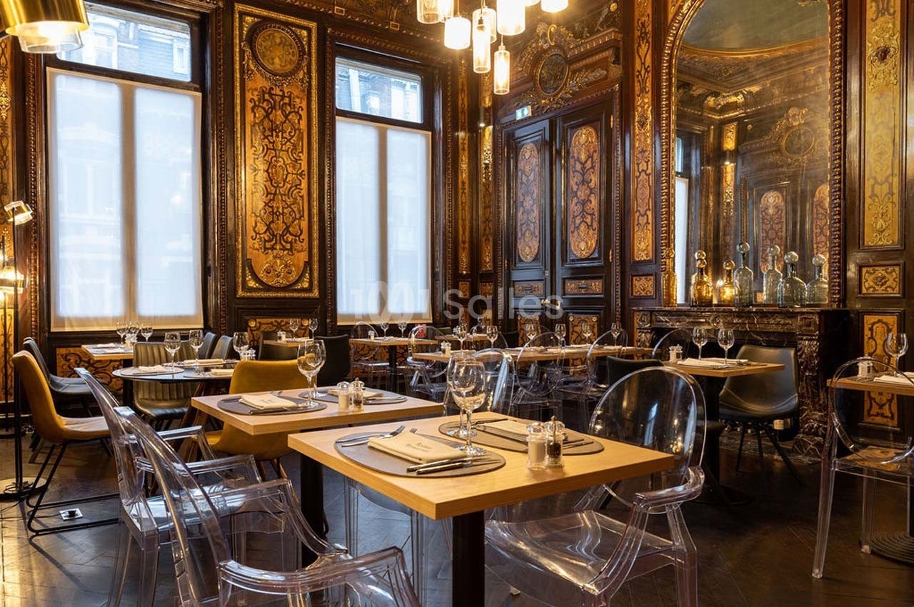 Salle de restaurant élégante avec décorations murales ornées, grandes fenêtres et mobilier moderne en bois et plastique…