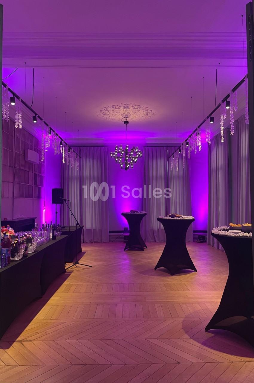 Salle élégante avec éclairage violet, tables hautes drapées de noir et buffet disposé sur le côté.