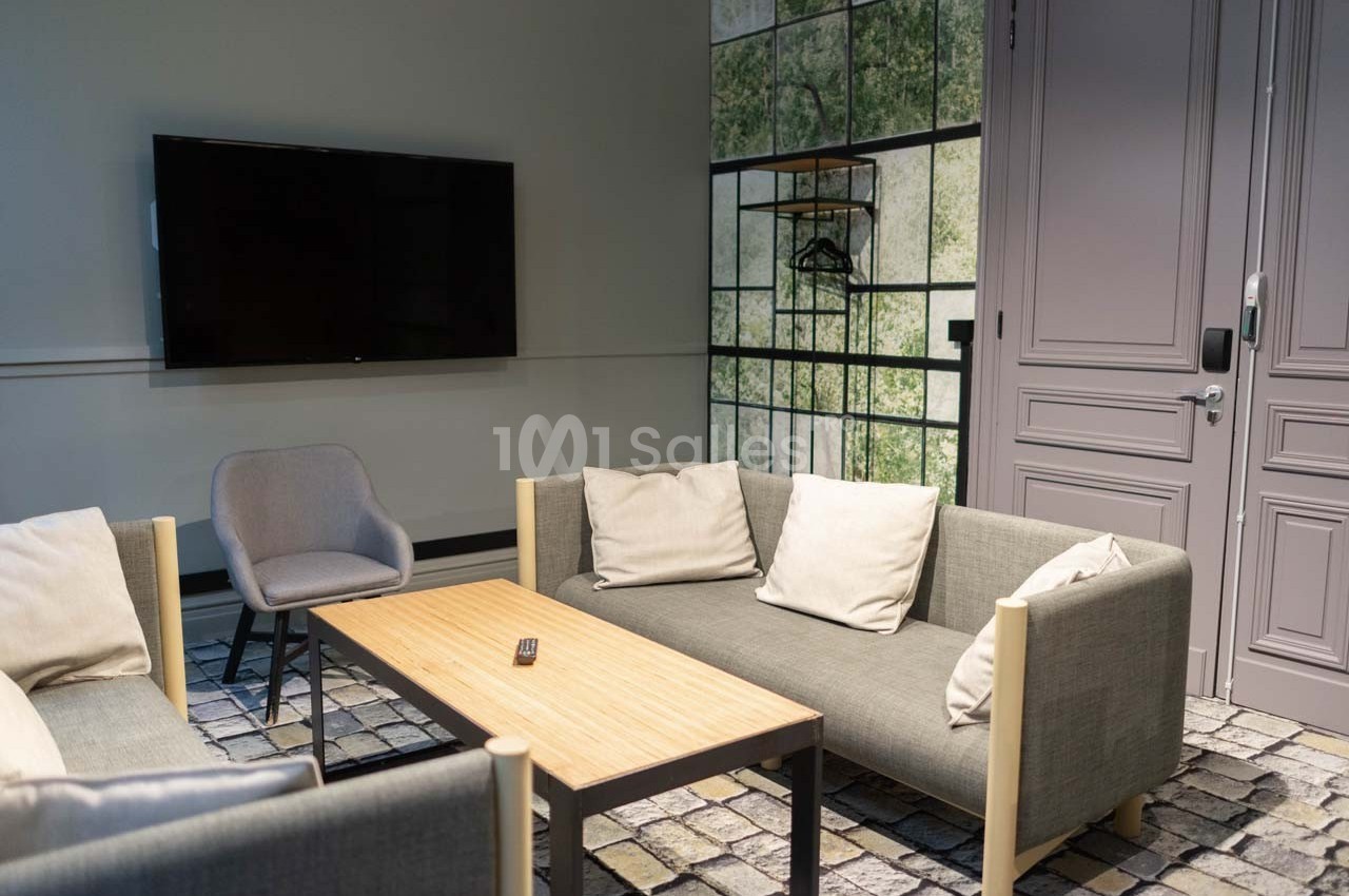 Salon moderne avec deux canapés gris, une table basse en bois, un fauteuil, un écran mural et une porte violette.