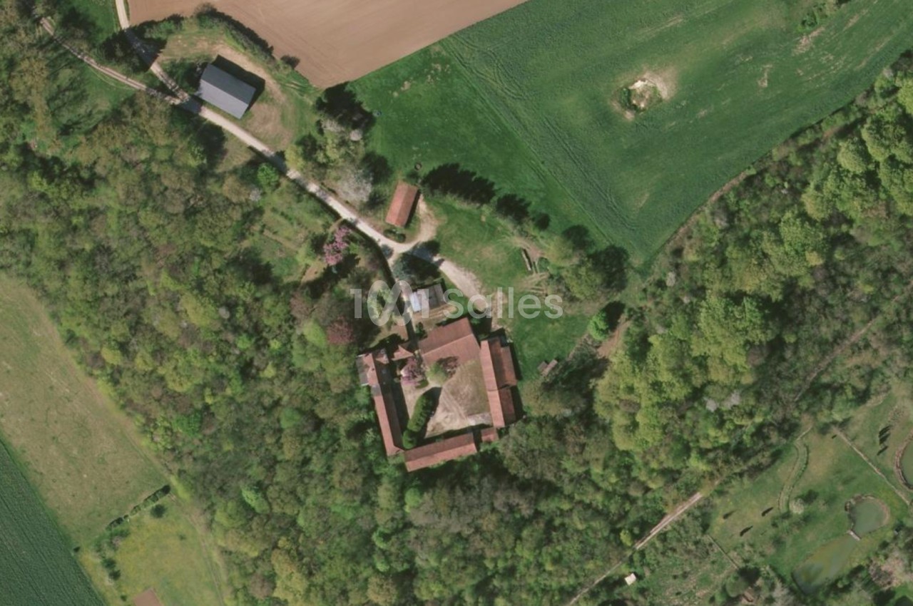 Vue aérienne d'un domaine entouré de forêts et de champs, avec plusieurs bâtiments et chemins visibles.