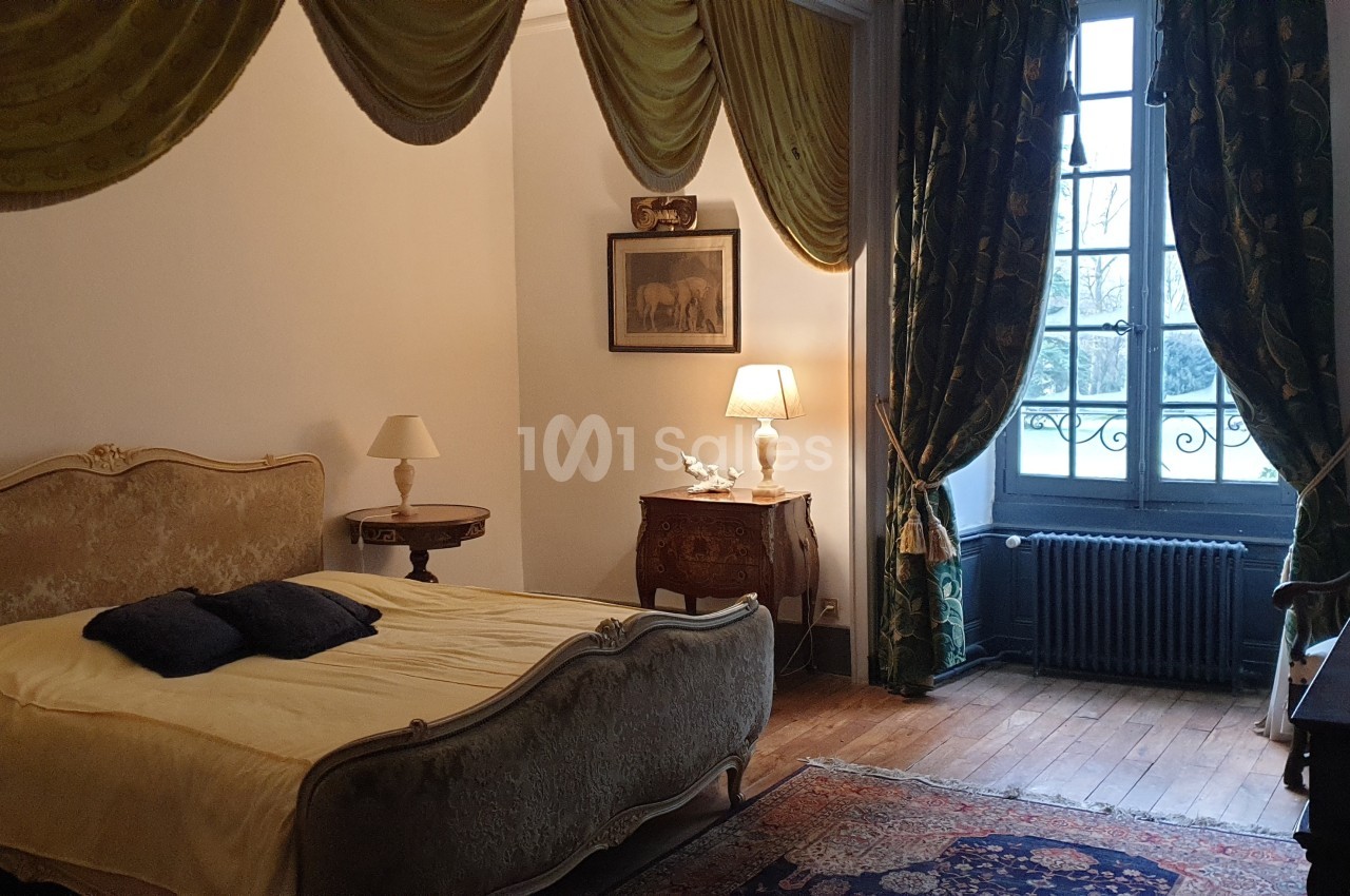 Chambre avec lit ancien, rideaux dorés, mobilier d'époque et fenêtre donnant sur un extérieur arboré.
