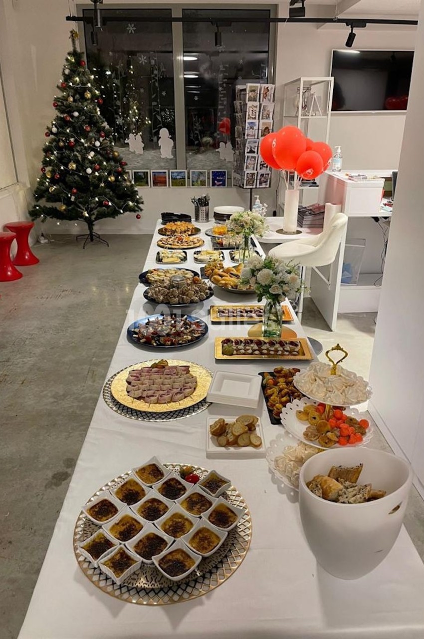 Table garnie de divers plats et desserts dans une salle décorée avec un sapin de Noël et des ballons rouges.