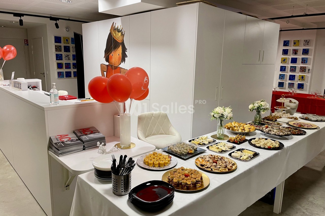 Table garnie de plats variés pour un buffet, avec des ballons rouges et une décoration murale illustrée en arrière-plan.