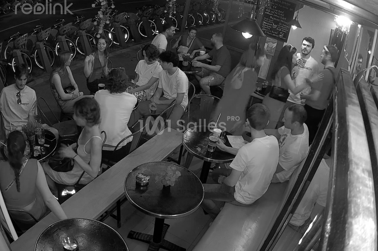 Des personnes discutent et partagent un moment convivial dans un bar animé, capturé en noir et blanc.